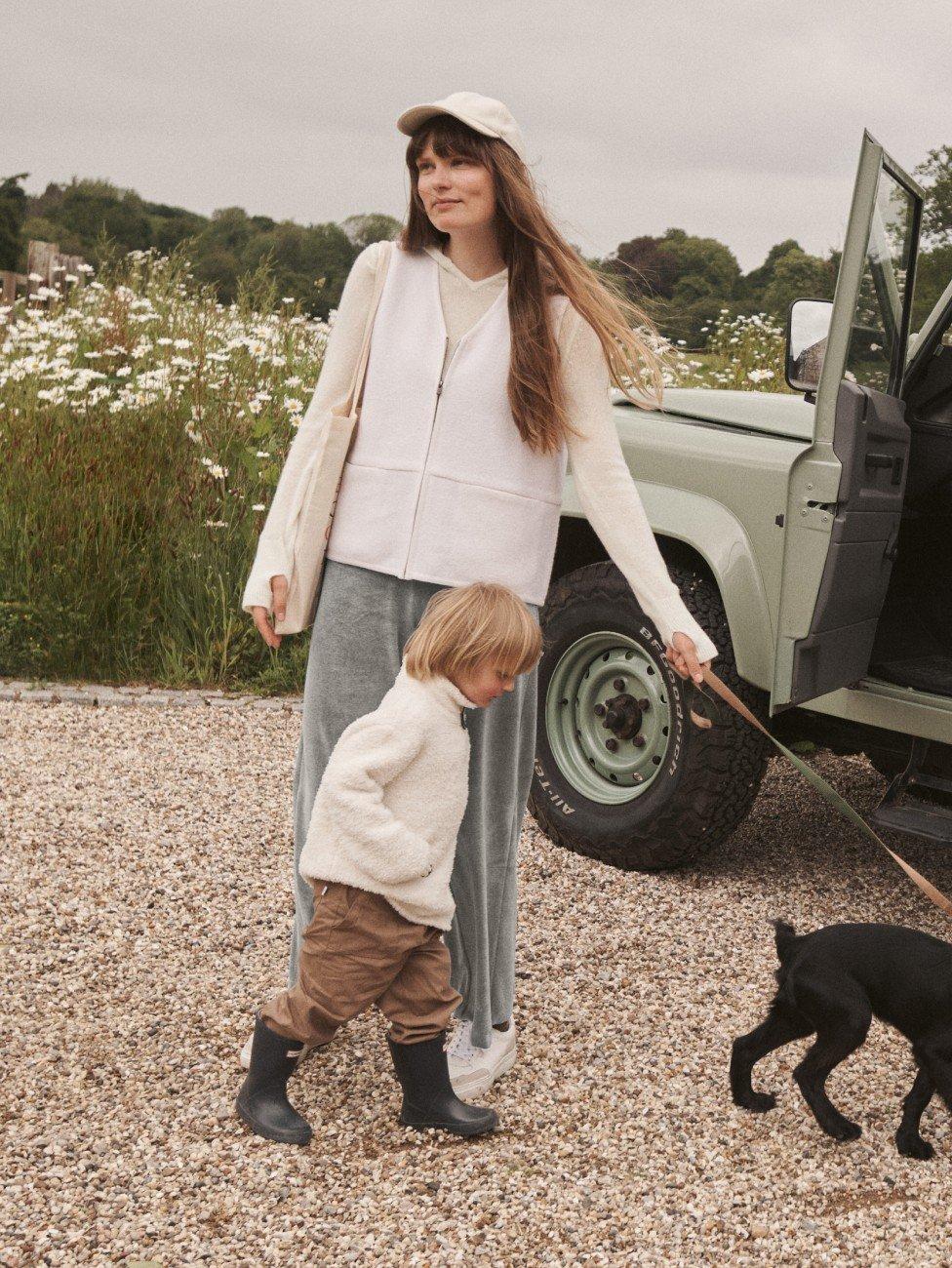 a woman and child walking a dog near a vehicle