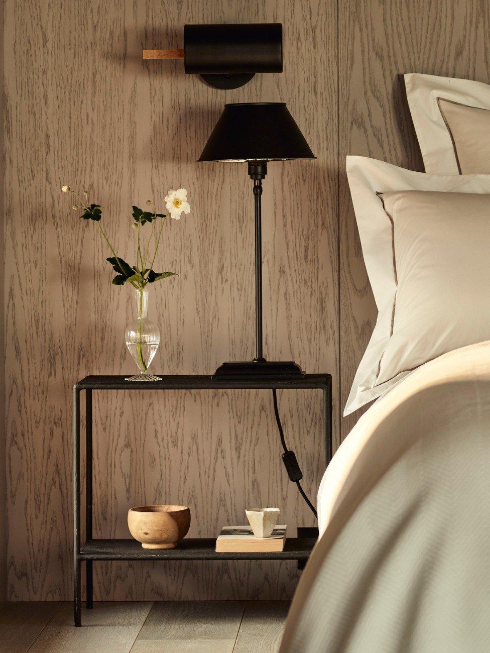 a bed with a night stand and a vase of flowers