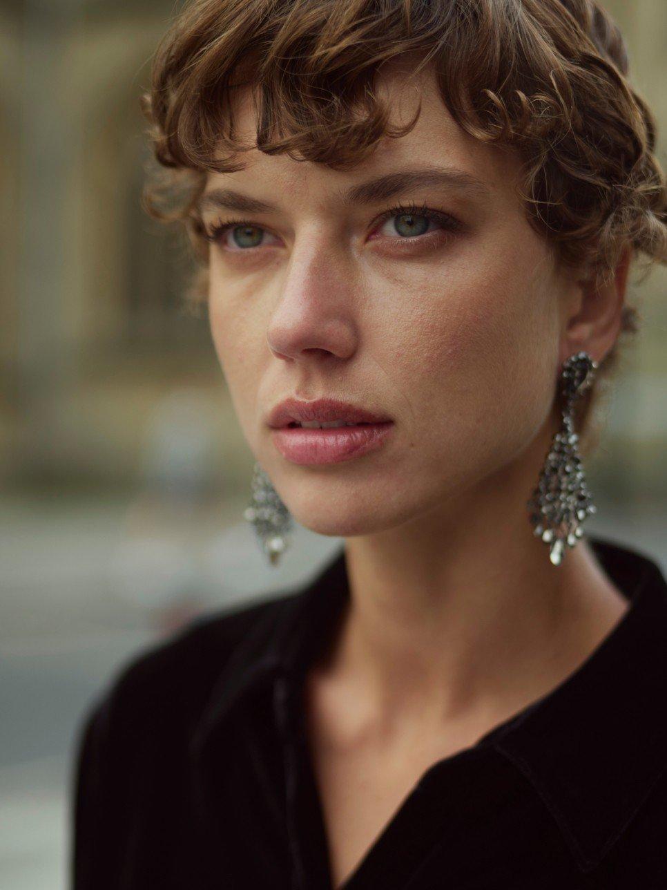 a woman with short curly hair wearing earrings and a black shirt