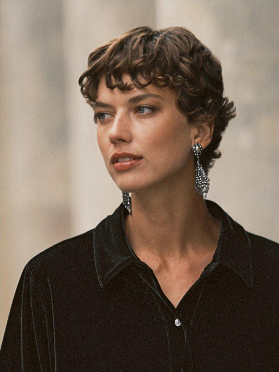 a woman with short hair wearing a black shirt and earrings