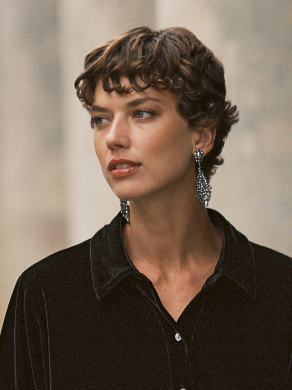 a woman with short hair wearing a black shirt and earrings