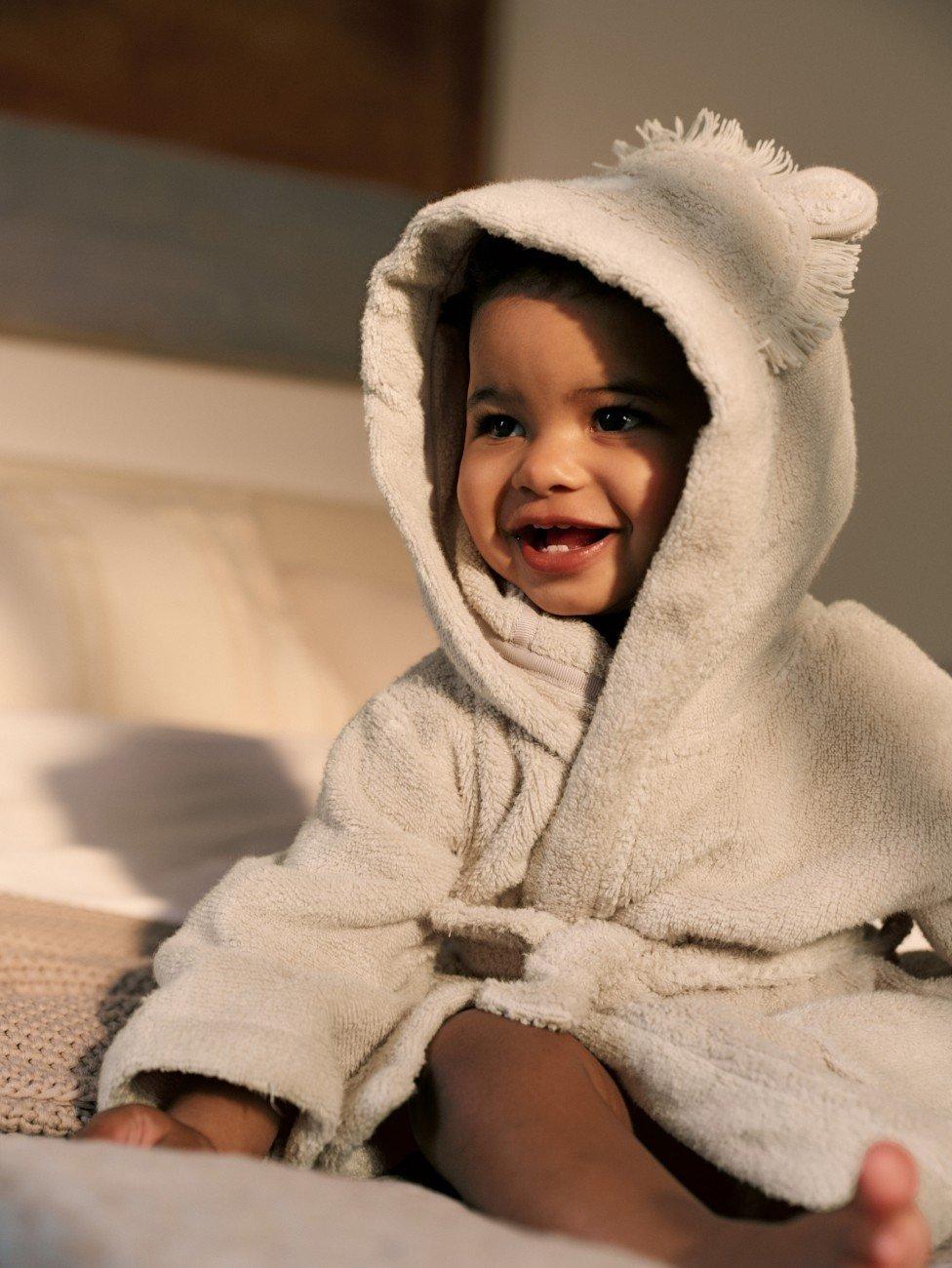 a baby in a robe sitting on a bed smiling