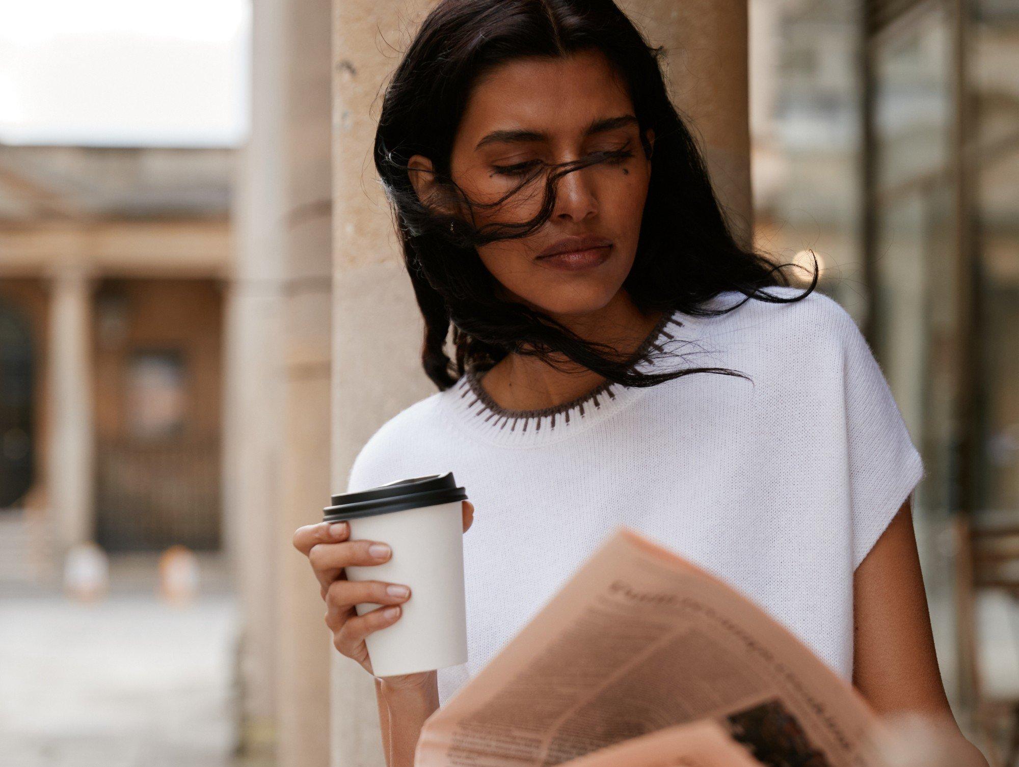 a woman with a coffee and a newspaper on a street