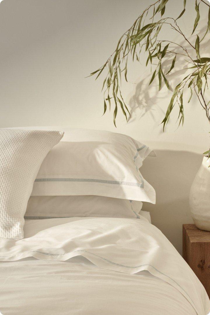 a white bed with white sheets and pillows and a vase of flowers