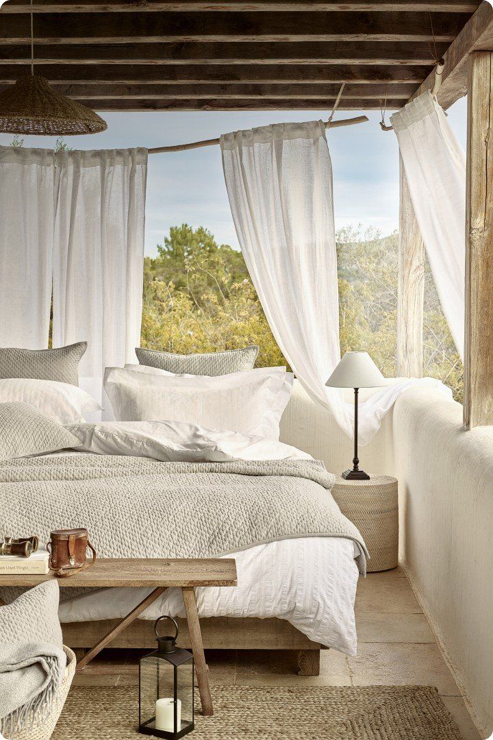 a bed with white sheets and pillows in a room with a window
