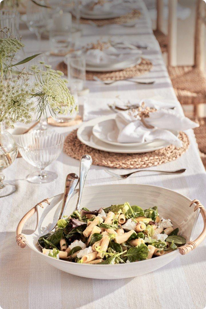 a white bowl filled with salad sits on a table with silverware