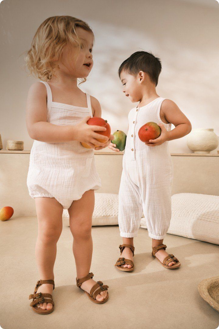 two children in white outfits holding apples and looking at each other
