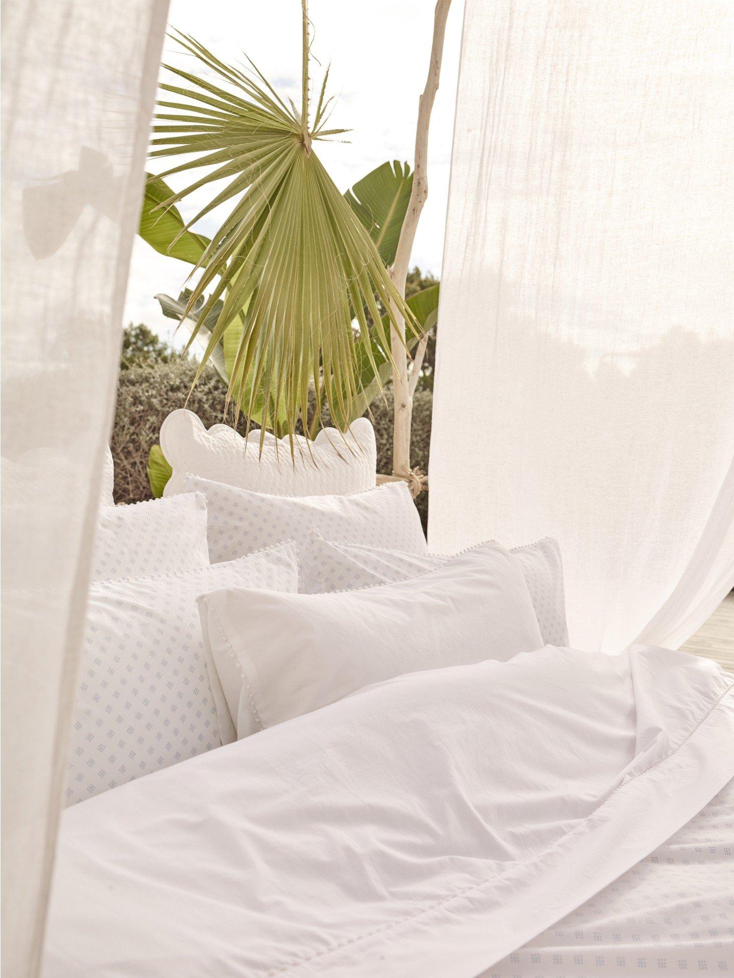 a bed with white sheets and a plant on top of it