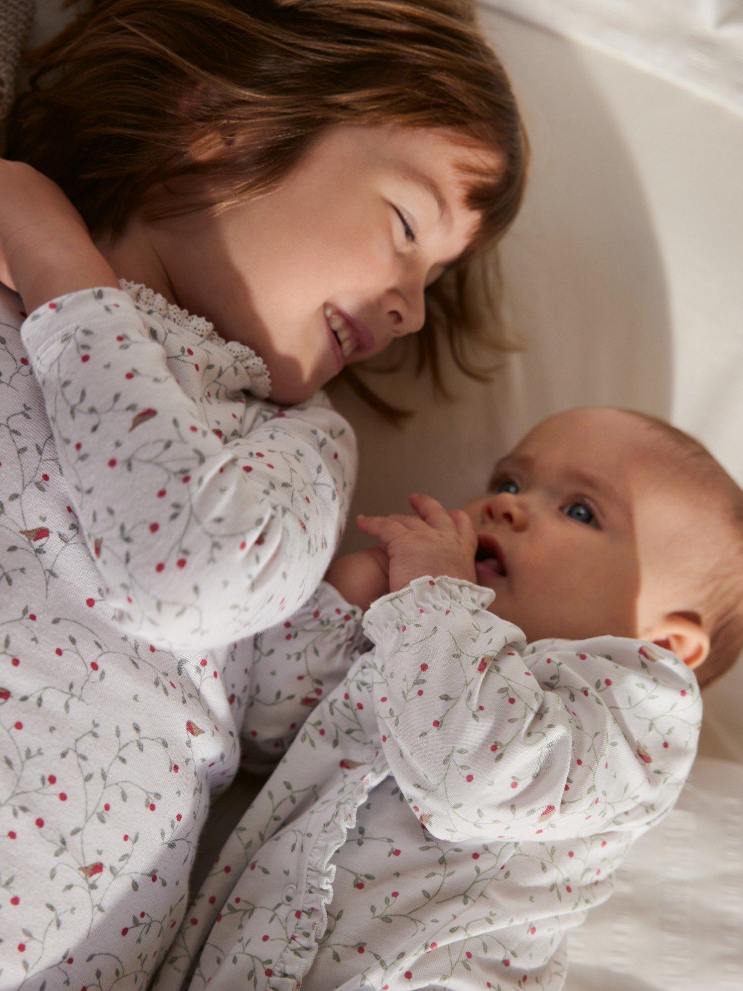 a baby girl and baby boy laying on a bed together