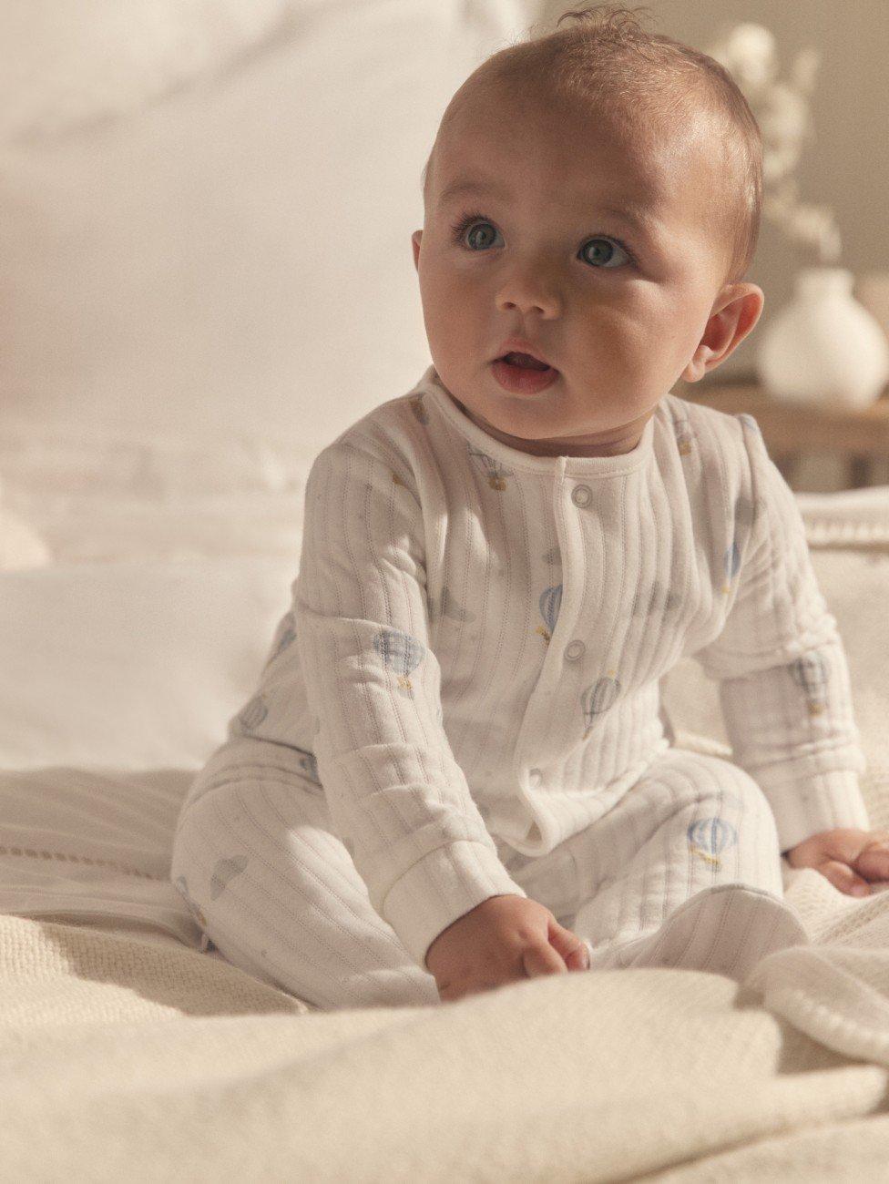 a baby sitting on a bed with a blanket on it