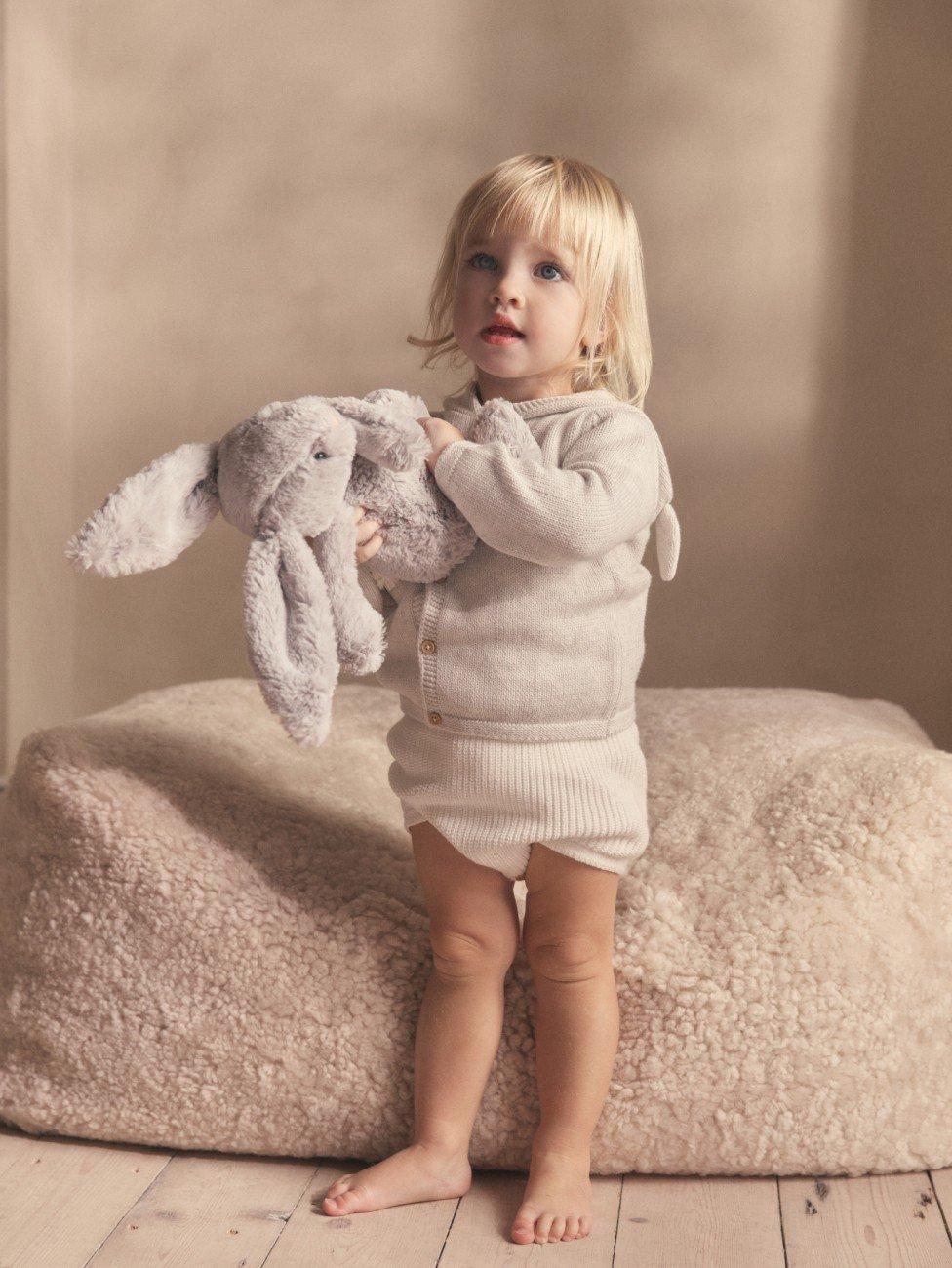 a little girl holding a stuffed animal in front of a wall