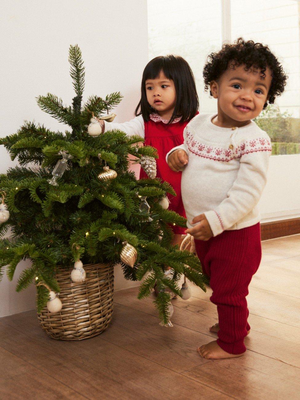 two children standing next to a small christmas tree in a room