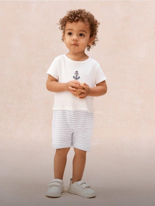 a young boy in a white shirt and shorts standing on a beige background