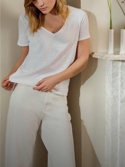 a woman in white pants and a white shirt standing by a vase