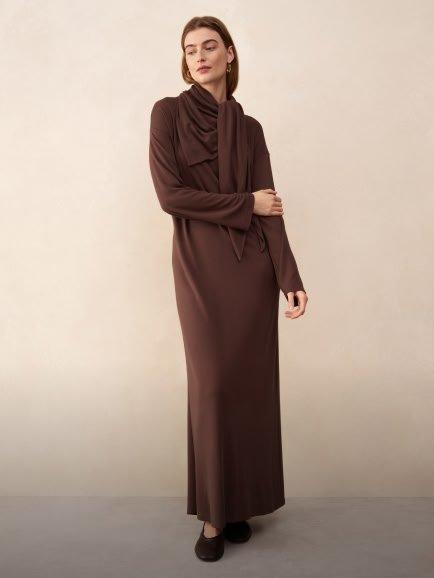 a woman in a brown dress standing against a wall