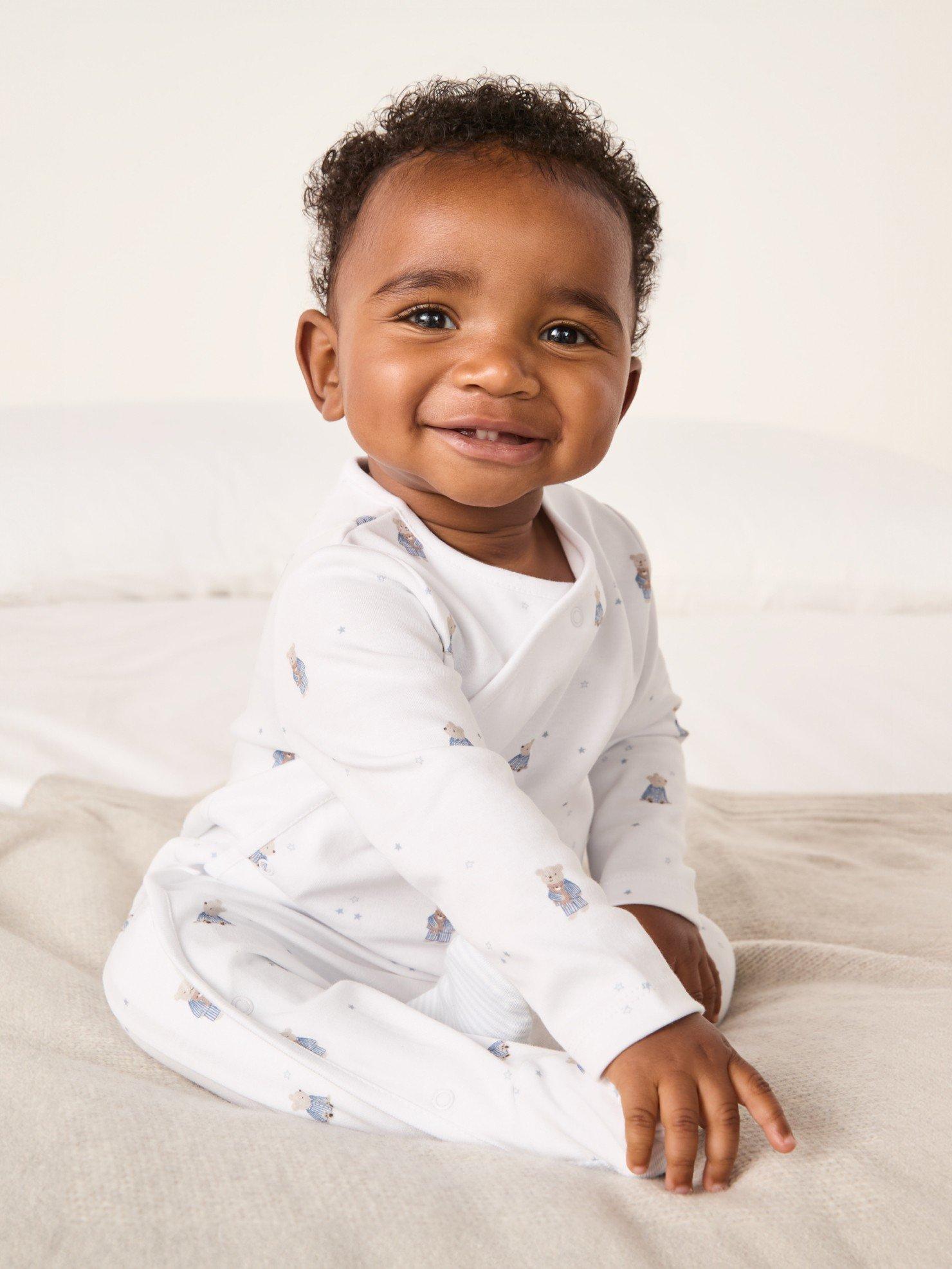 a baby sitting on a bed smiling at the camera