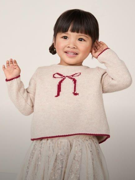 a little girl in a white sweater and a red bow on her head