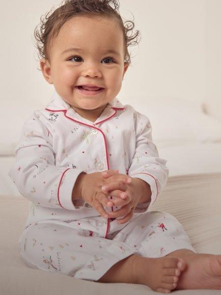 a baby in pajamas sitting on a bed smiling