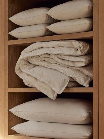 a closet with a white shirt hanging on a hanger and a stack of white pillows