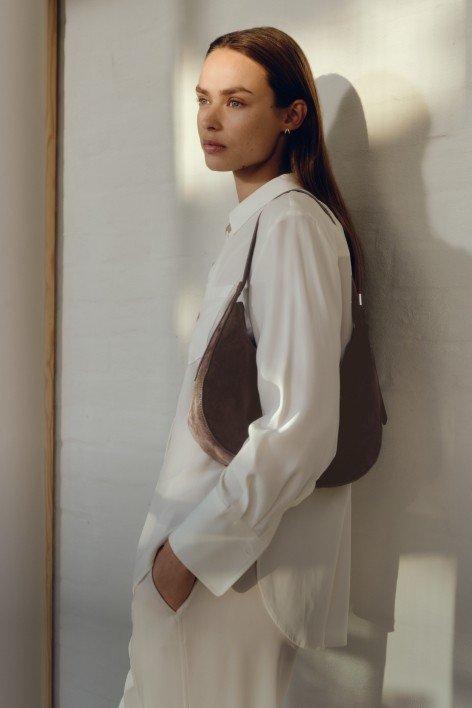 a woman in white standing against a wall with a purse