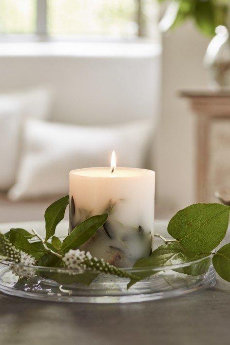 a candle on a glass table with a leaf and a flower