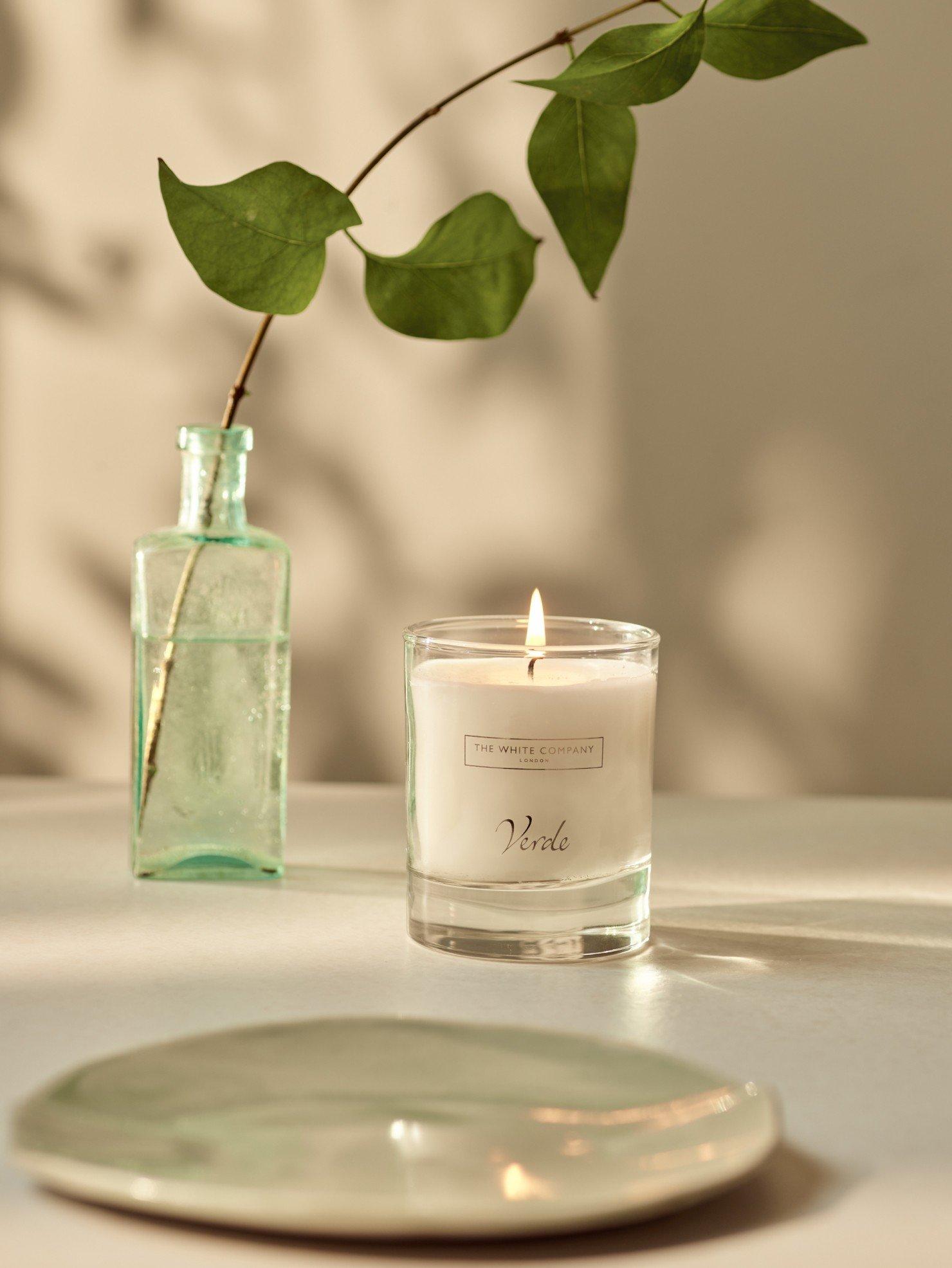 a candle and a vase on a table with a leaf