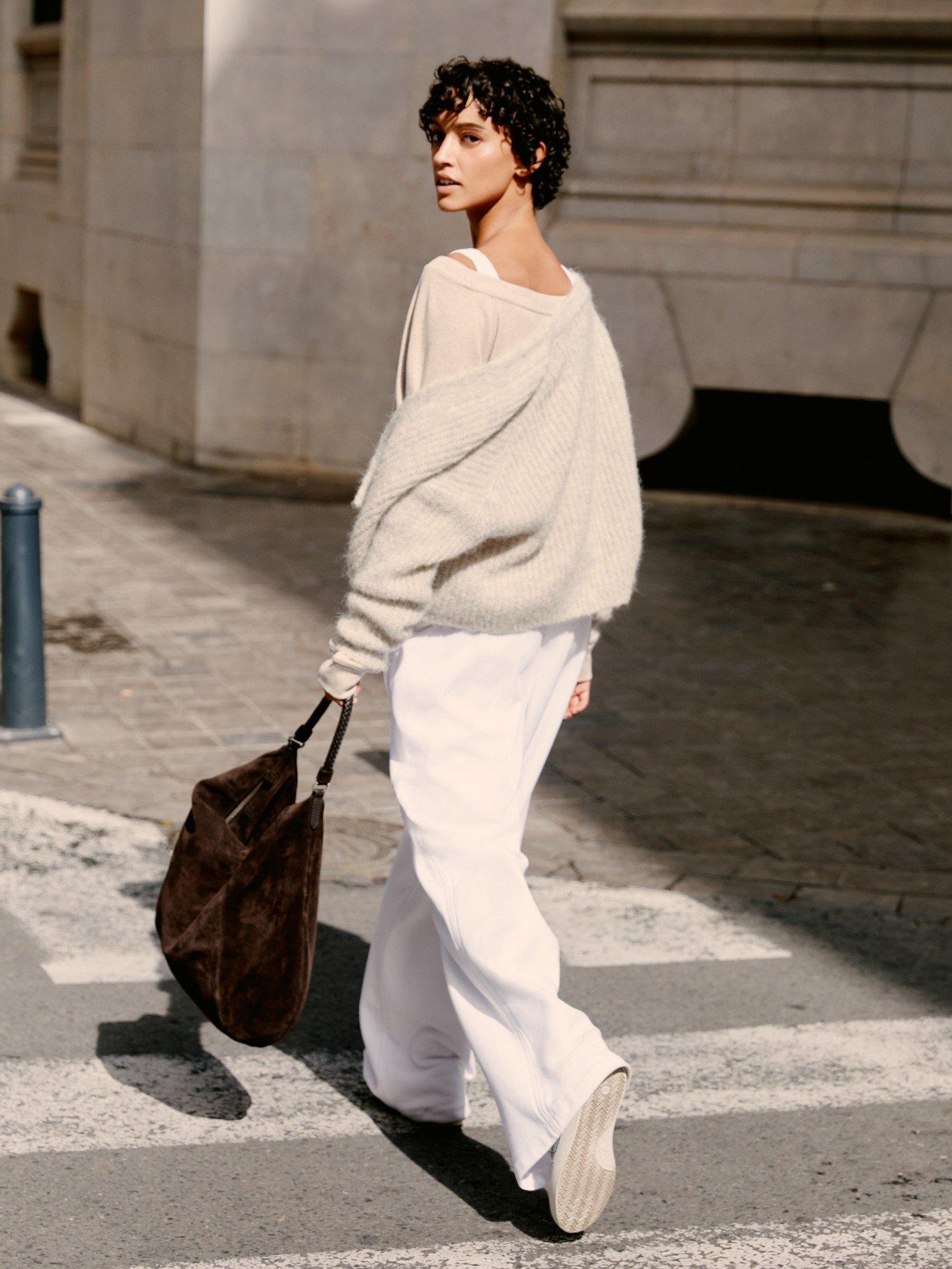 a woman in white pants and sweater walking across a street