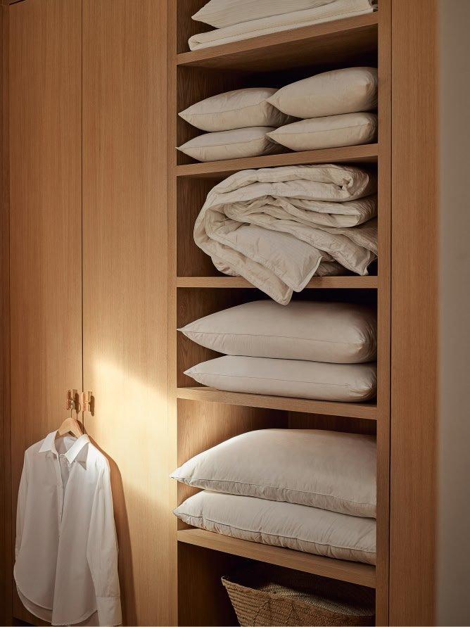 a closet with a white shirt hanging on a hanger and a stack of white pillows
