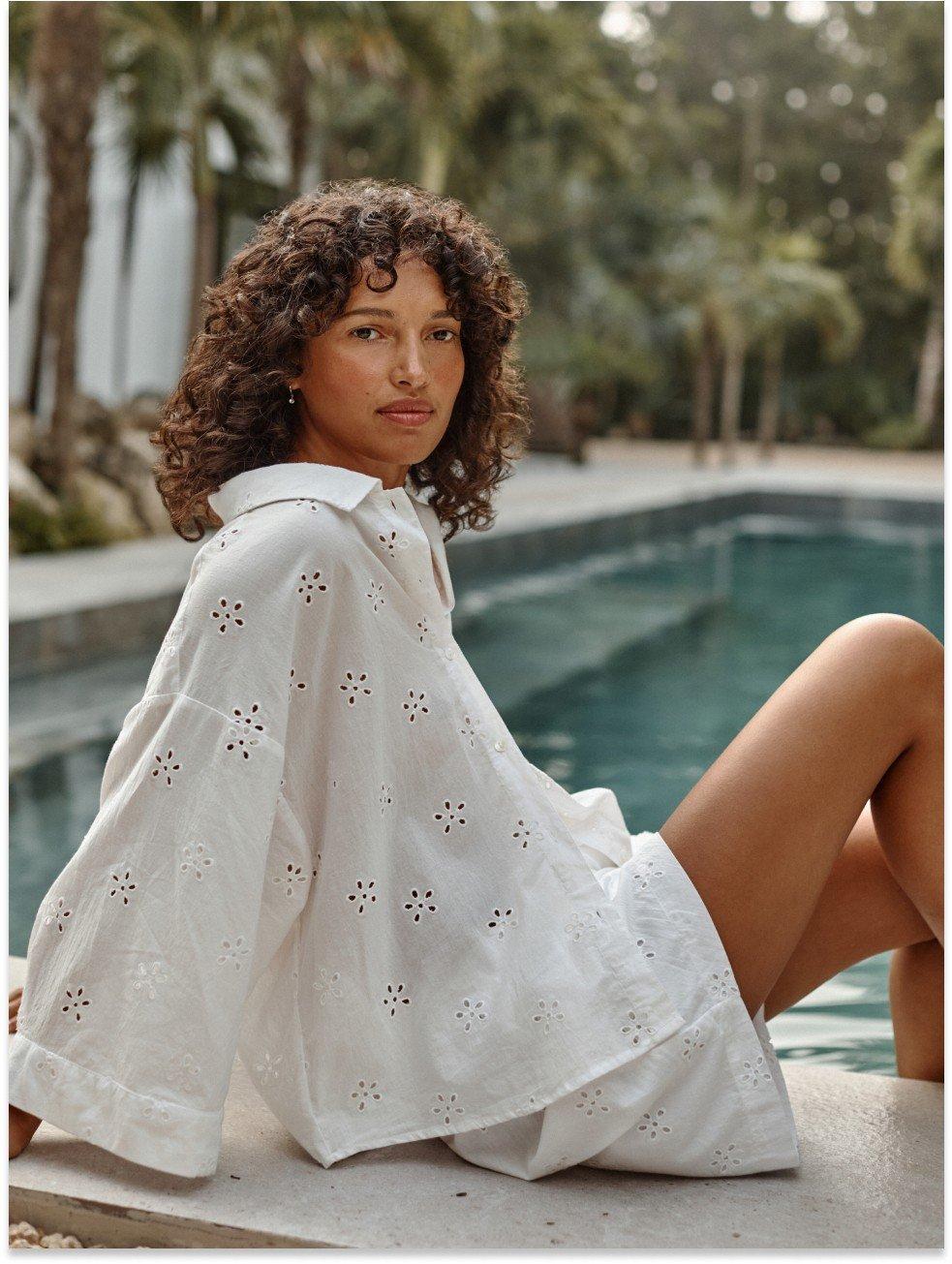 a woman in white pyjamas sitting by a pool