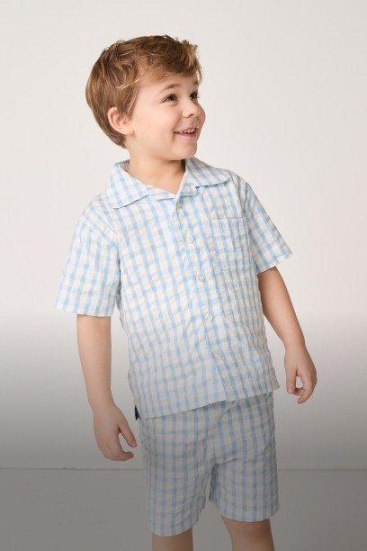 a young boy in a blue and white checkered shirt and shorts