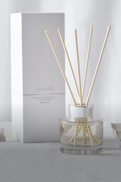a white reed diffuser with sticks in front of a box