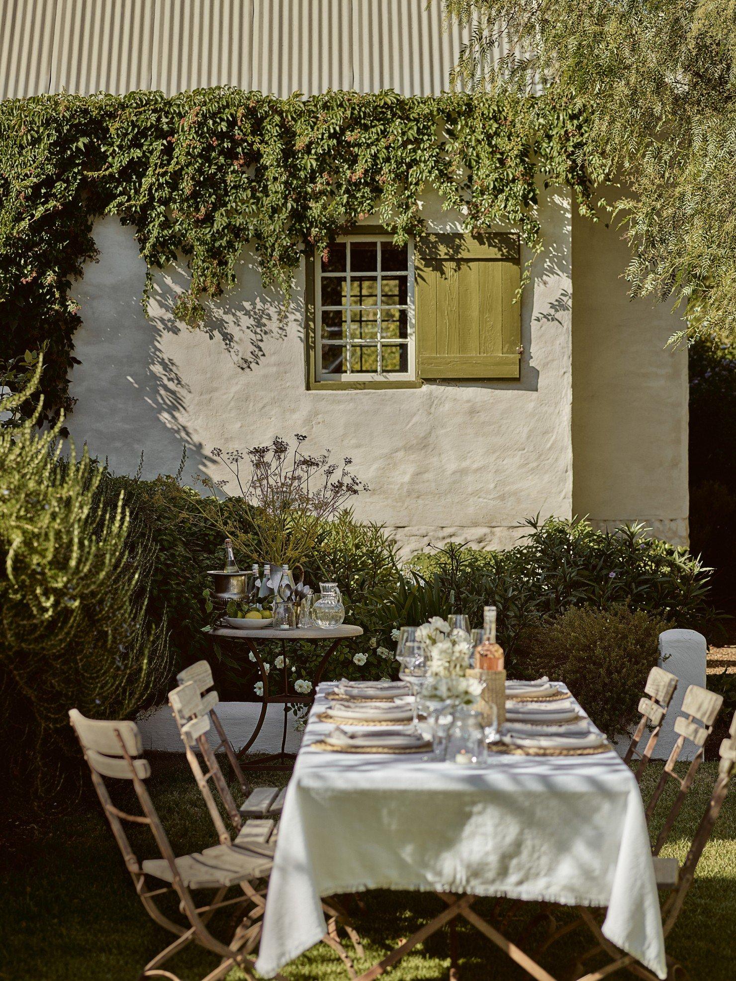 a table set up in the backyard with chairs and a vase of flowers