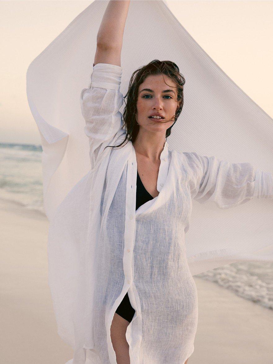 a woman in a white shirt standing on a beach holding a white cloth