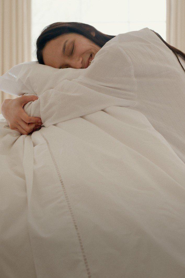 a woman laying in bed with a white comforter and white sheets