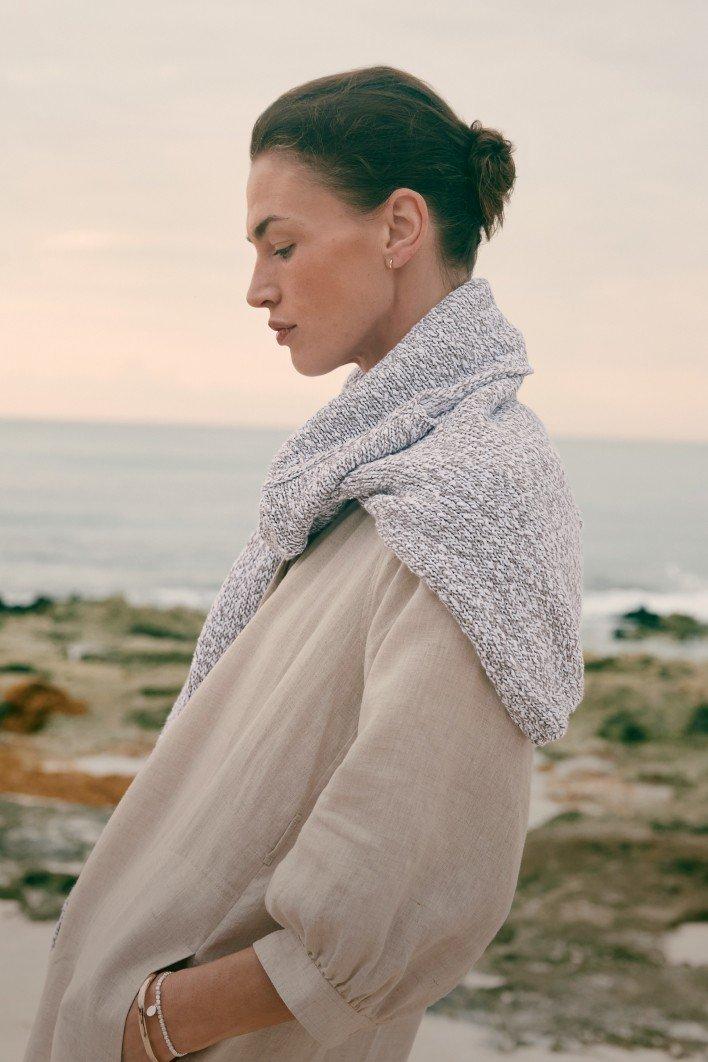 a woman standing on a beach with a jumper over her shoulders