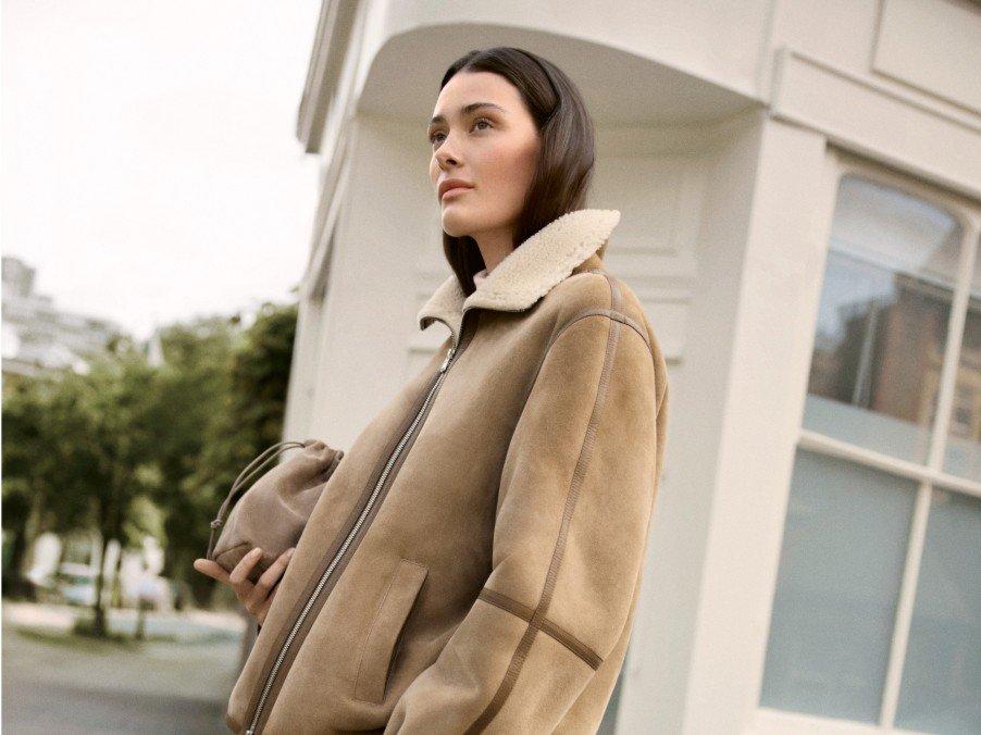 a woman in a brown jacket and skirt standing outside