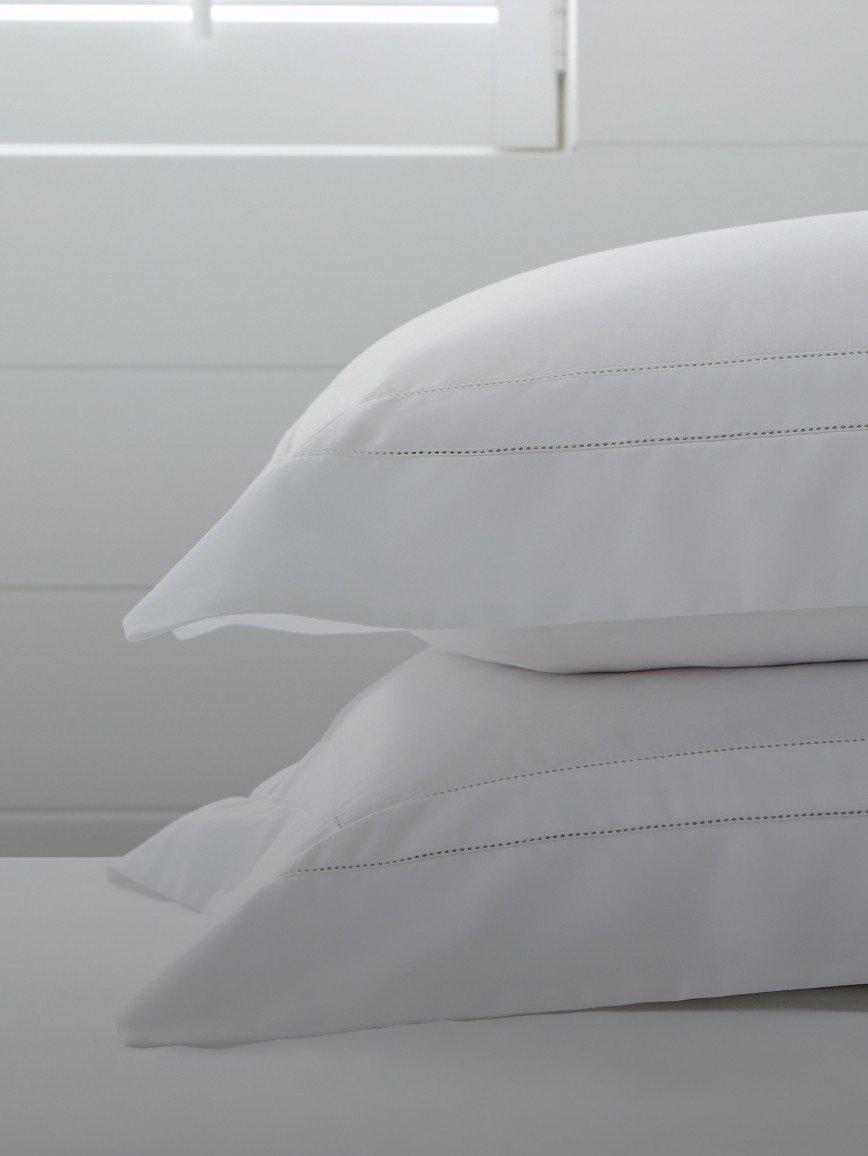 two white pillows sitting on top of a bed with a window