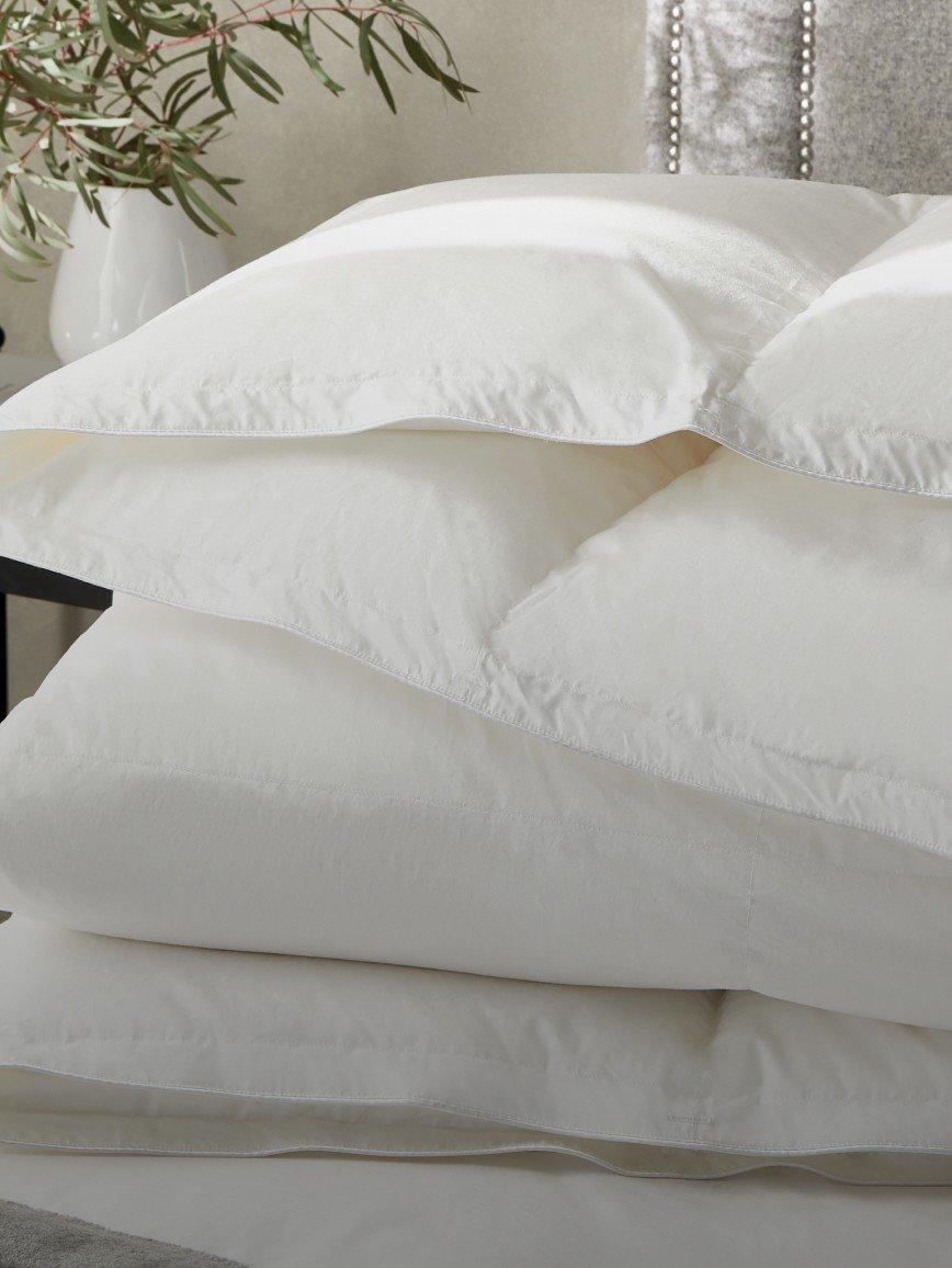 a stack of white pillows on top of a bed with a plant
