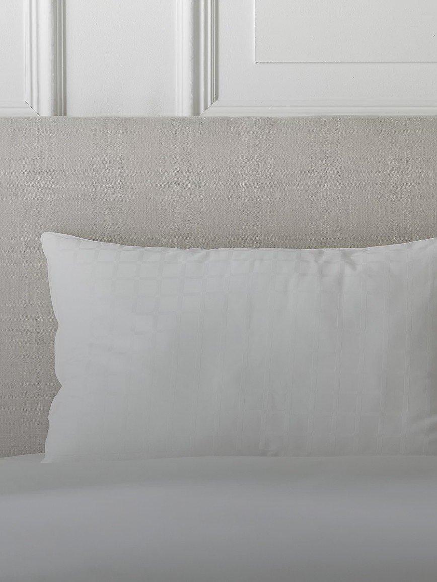 a white pillow on a bed with a white headboard