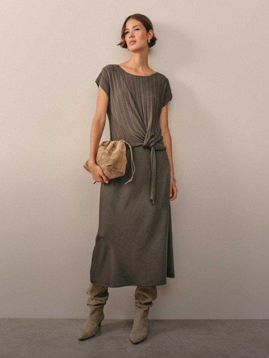 a woman in a grey dress and boots standing against a wall