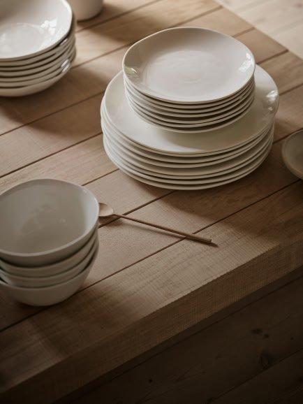 a table with many plates and bowls on it with a person putting food on them