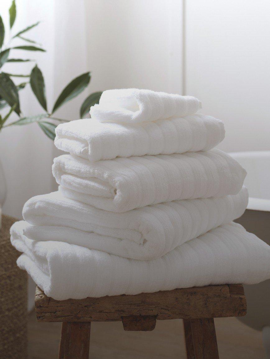 a stack of white towels sitting on a stool next to a bathtub