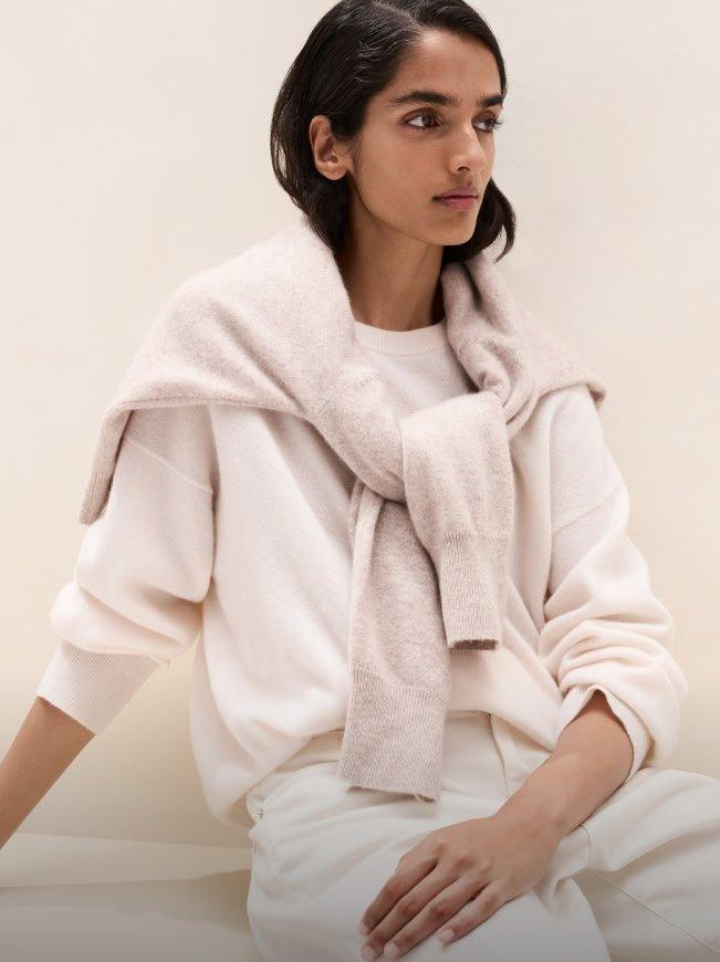 a woman in white sitting on a bench with a scarf around her neck