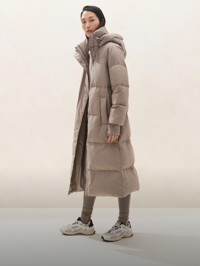 a woman in a long coat standing in a white room
