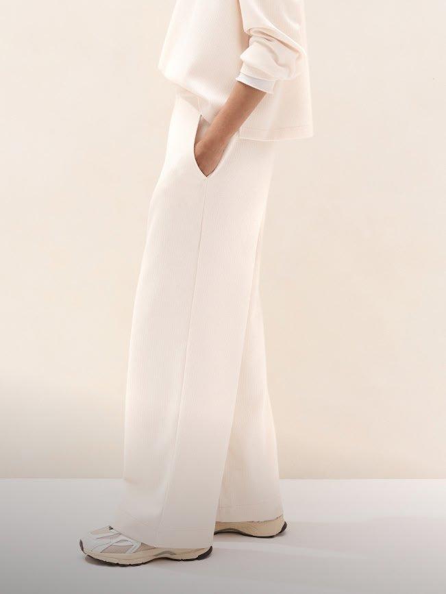 a woman in white jumpsuit standing in front of a wall