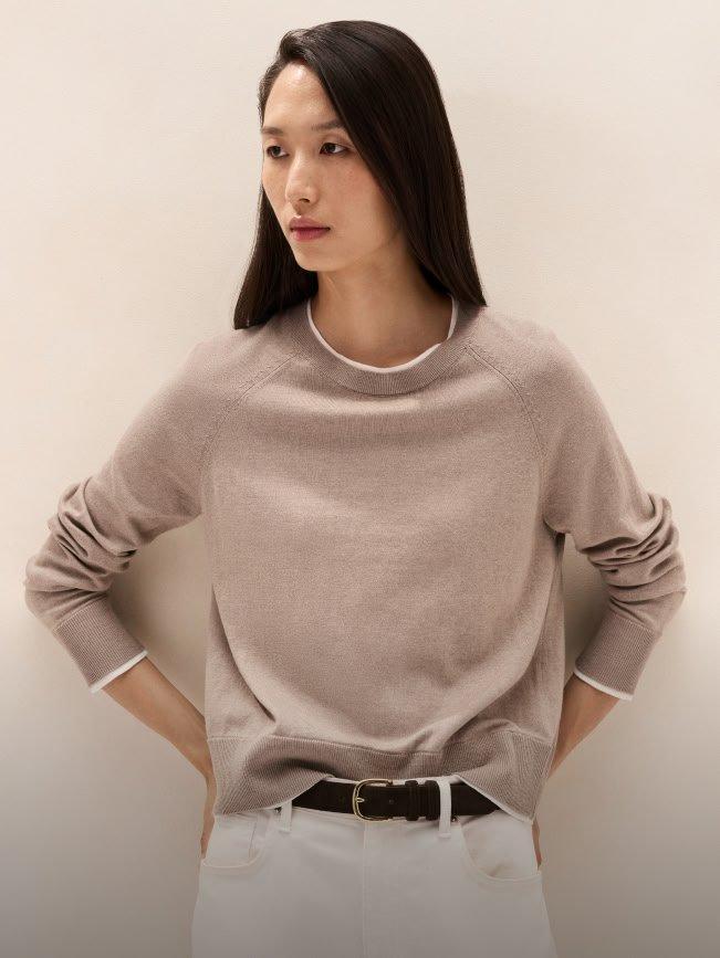 a woman in a sweater and white pants leaning against a wall