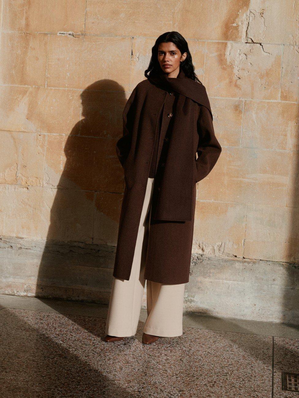 a woman in a grey sweater and a pleated skirt holding a scarf