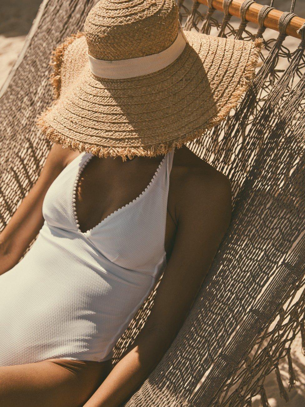 a woman in a white swimsuit and a straw hat on a hammock