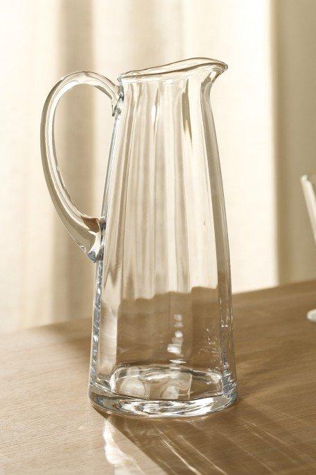 a clear glass pitcher sitting on a wooden table next to a glass