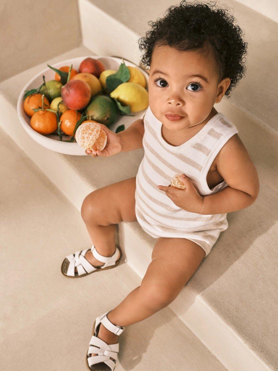 a baby sitting on steps with a bowl of fruit